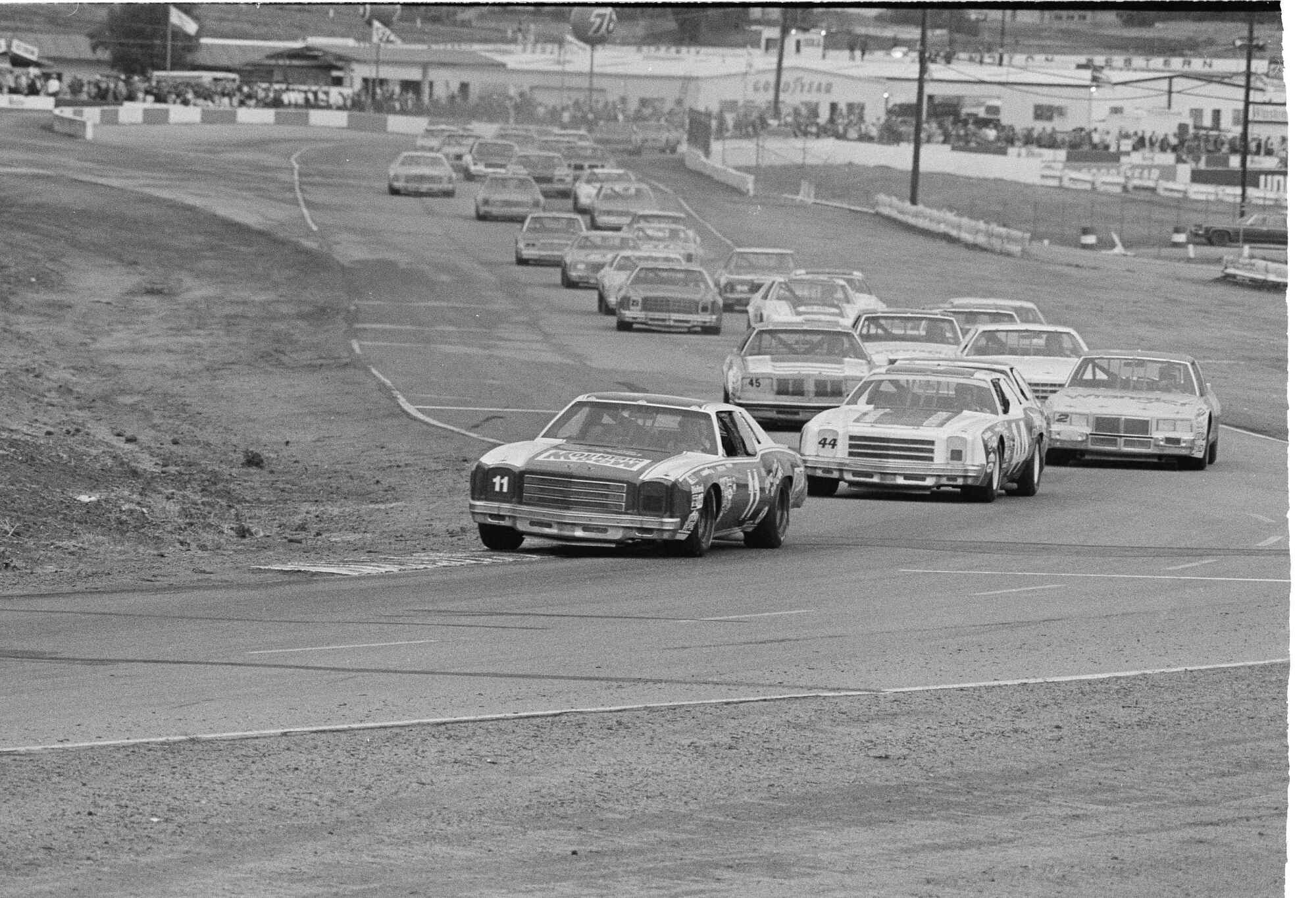Cars race around a track in a black-and-white photo from 1981.