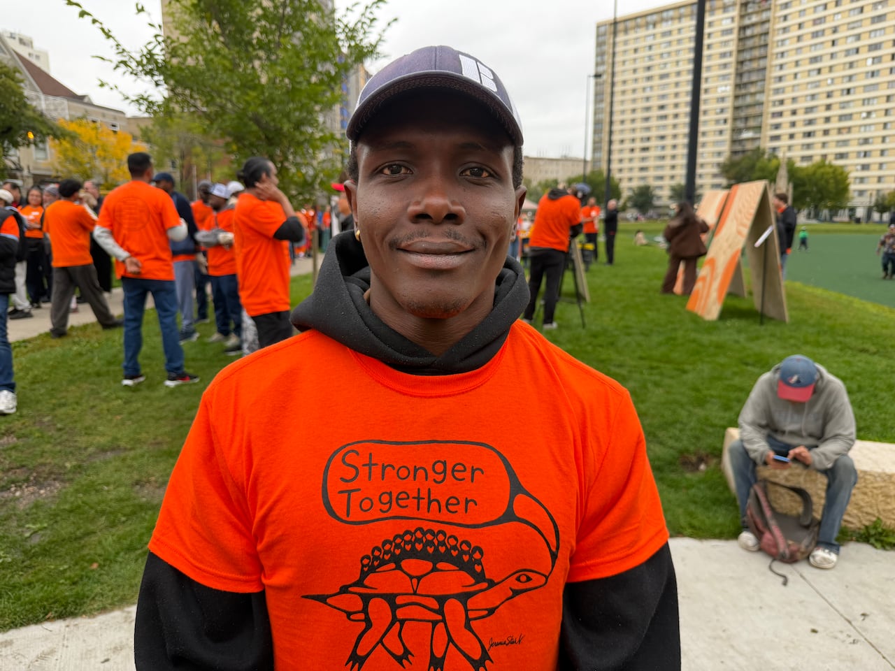 Man stands wearing an orange t-shirt with the words stronger together on the front.