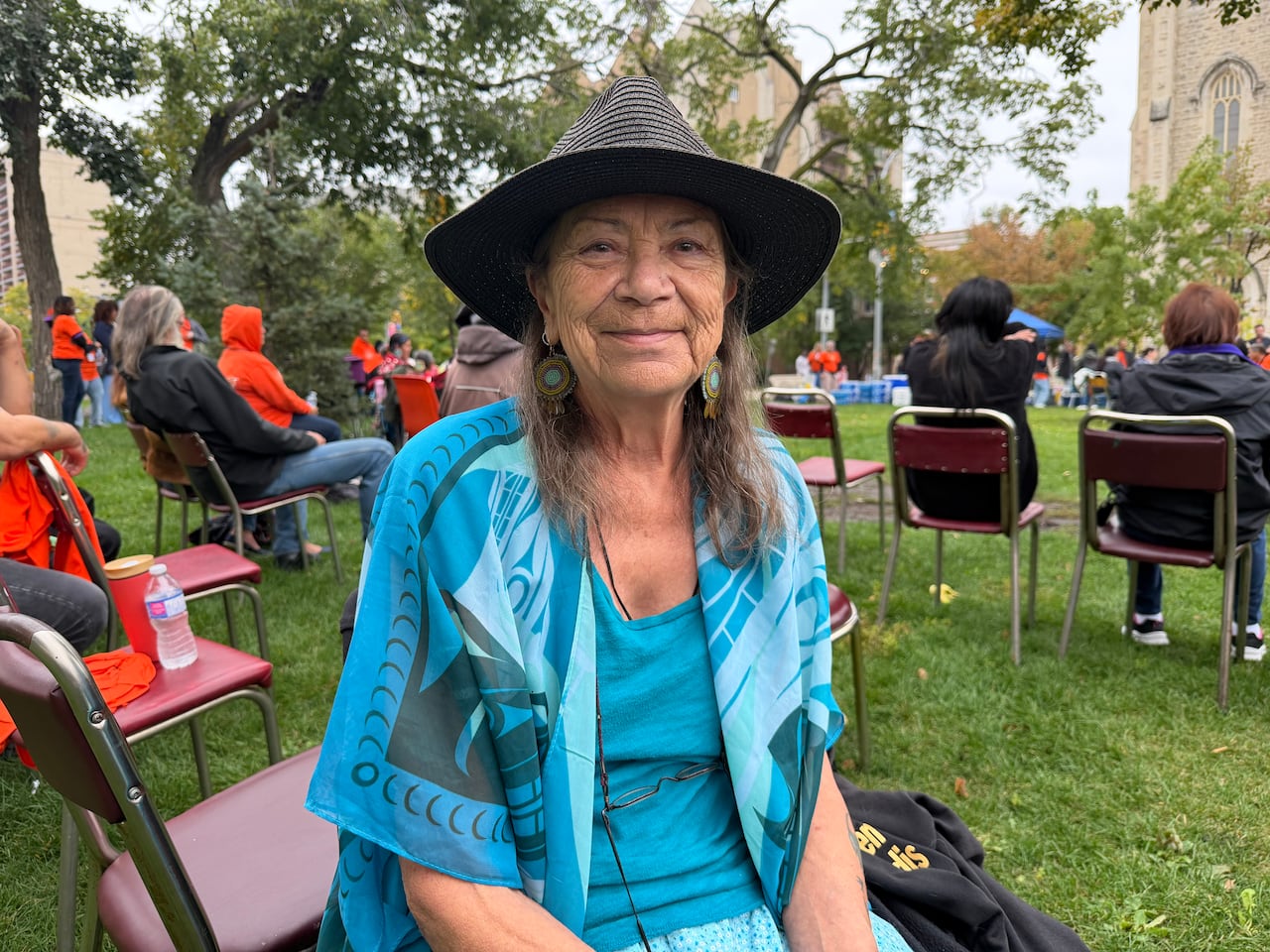 Woman with long hair wearing blue sits at an outdoor event.