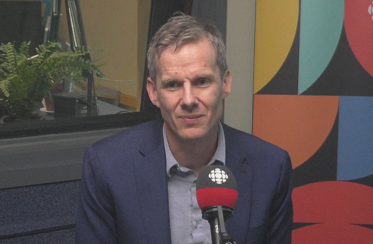 A man in a radio studio sits in front of a microphone with the CBC logo on it.