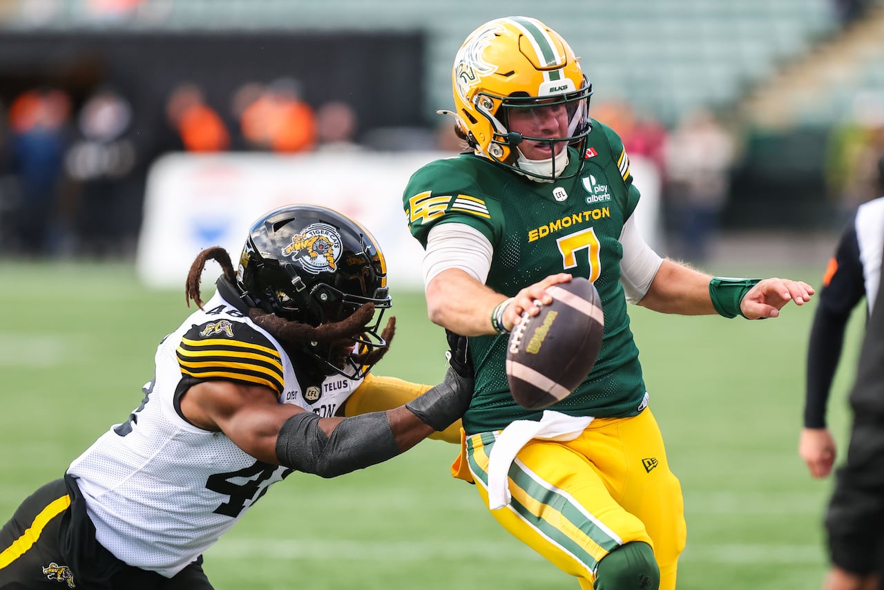 A men's football player, wearing a green-and-yellow uniform, runs with the ball, evading an opponent's tackle attempt.