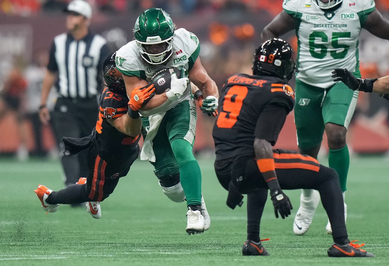 A man wearing a football uniform runs while holding a football as another man clings to his arm.