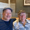 Two smiling men are shown; the younger man has his arm around his father's shoulders. 