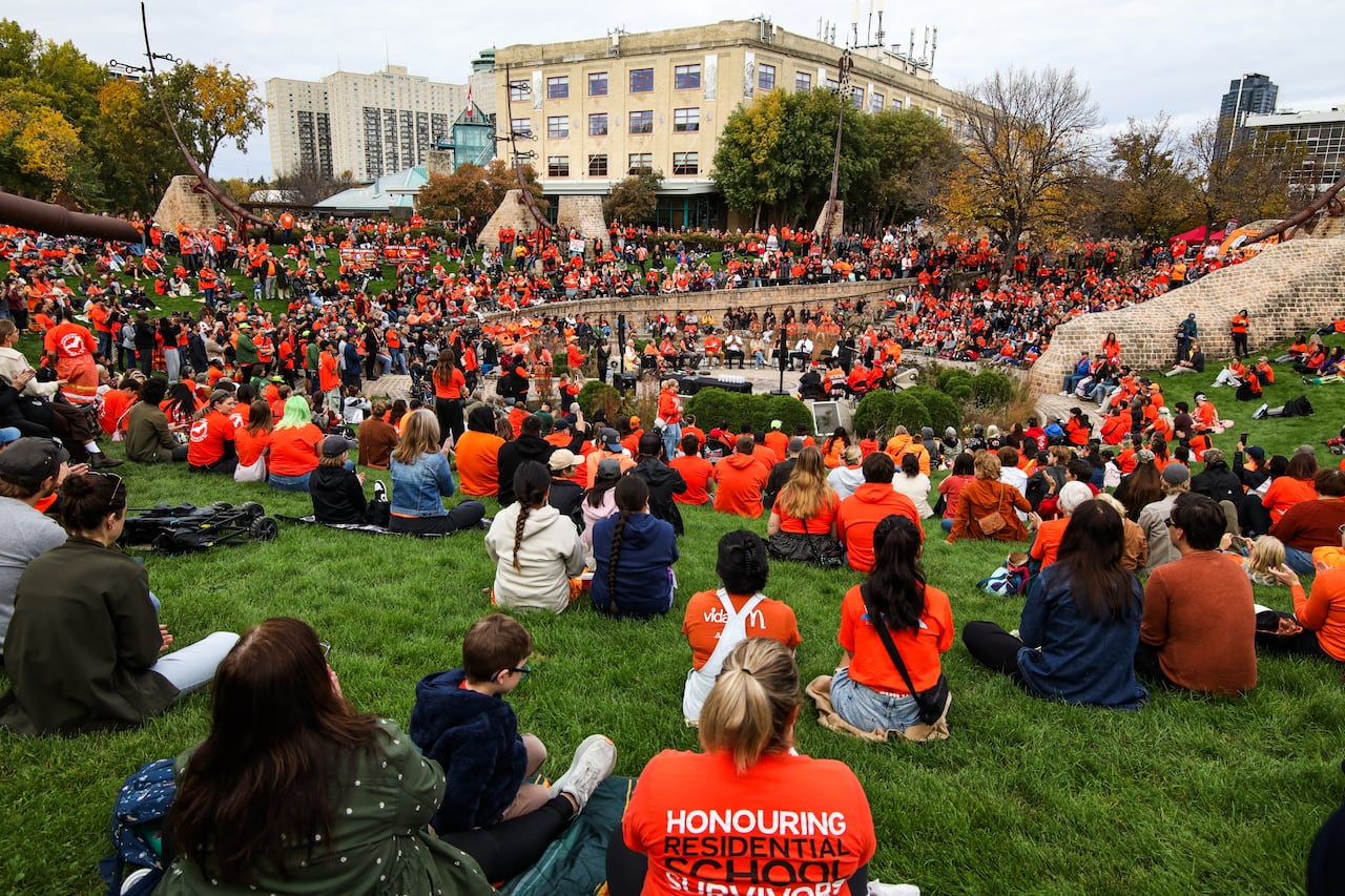 People wearing bright orange T-shirts and hoodies sit together outside.