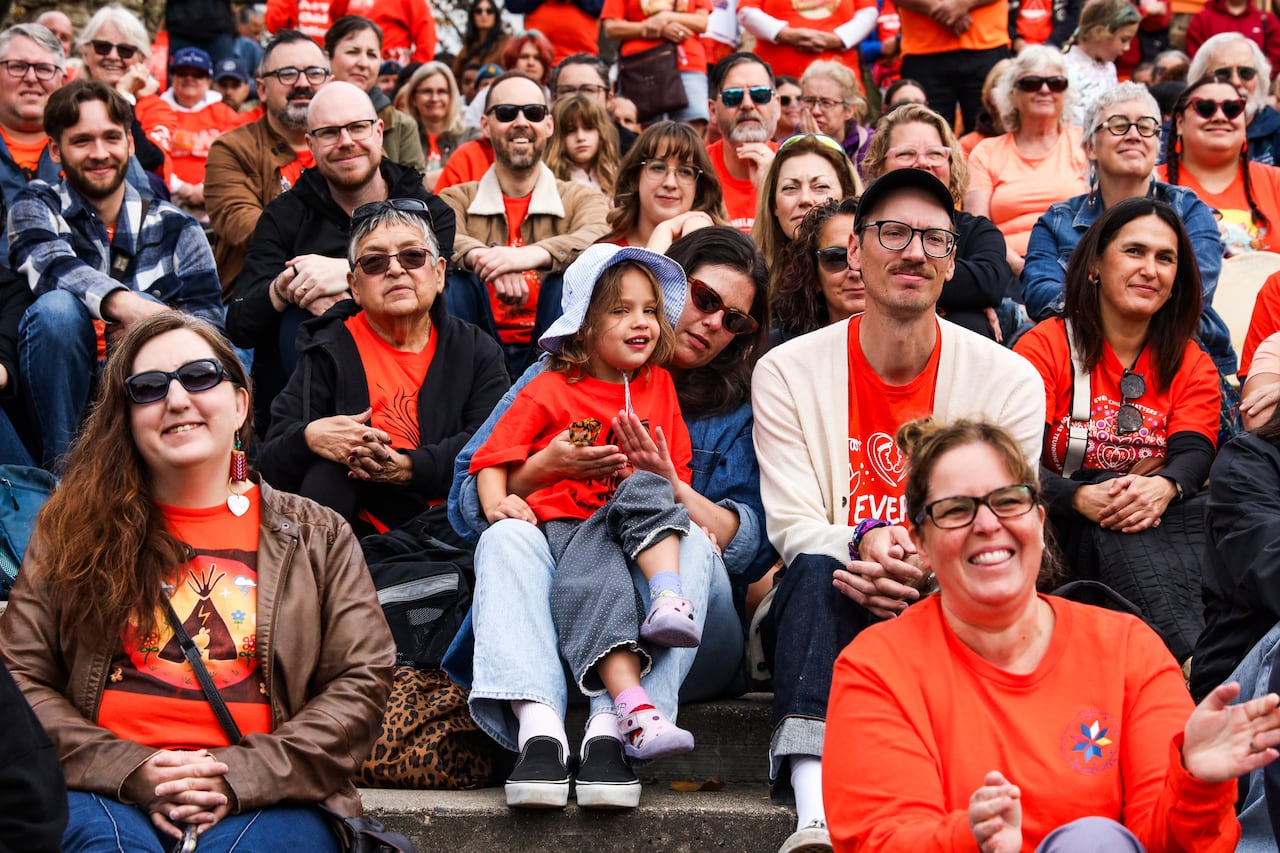 A woman holds a young child in a crowd sitting together wearing orange shirts.