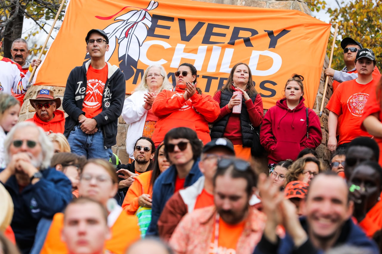 People wearing orange stand in from of a large flag reading 'Every Child Matters.'