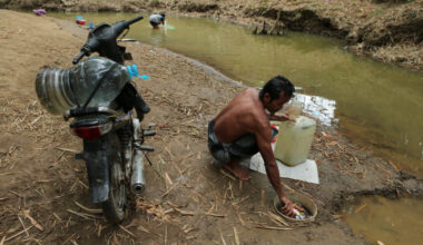 A man fills a water container from a river as water levels recede during the dry season amid drought conditions in Ridogal...