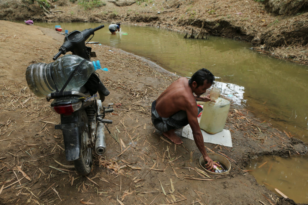 A man fills a water container from a river as water levels recede during the dry season amid drought conditions in Ridogal...