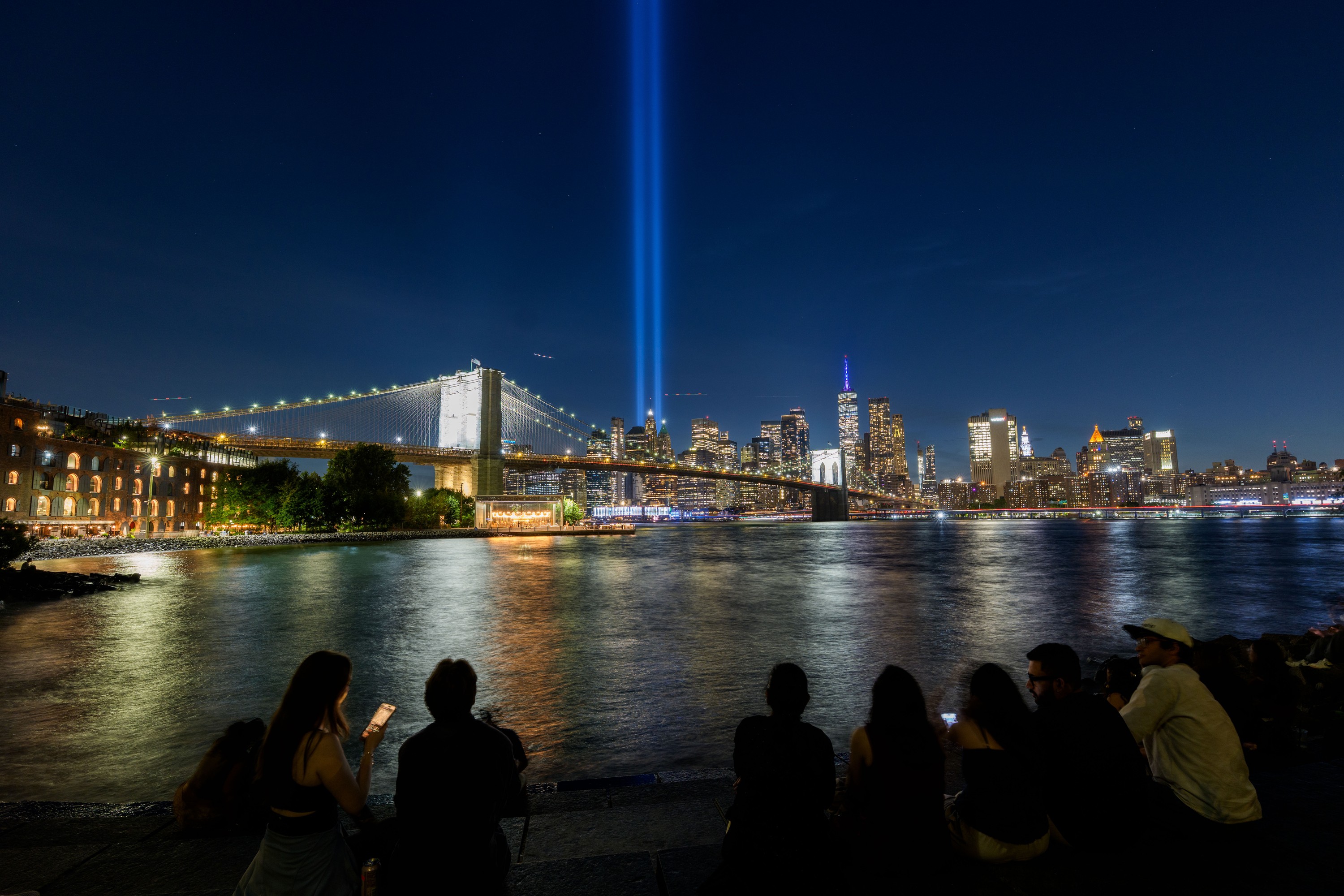 Two blue lights shine from New York City's skyline into the clouds.