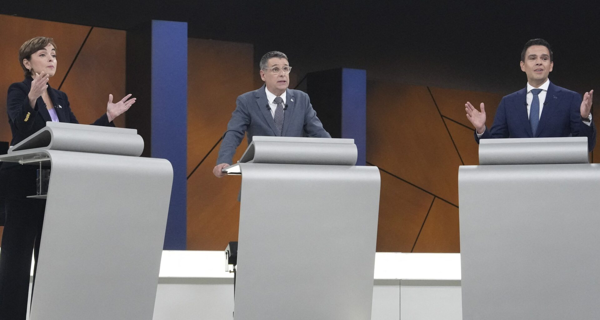 Three people standing at podiums during a debate
