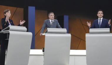 Three people standing at podiums during a debate