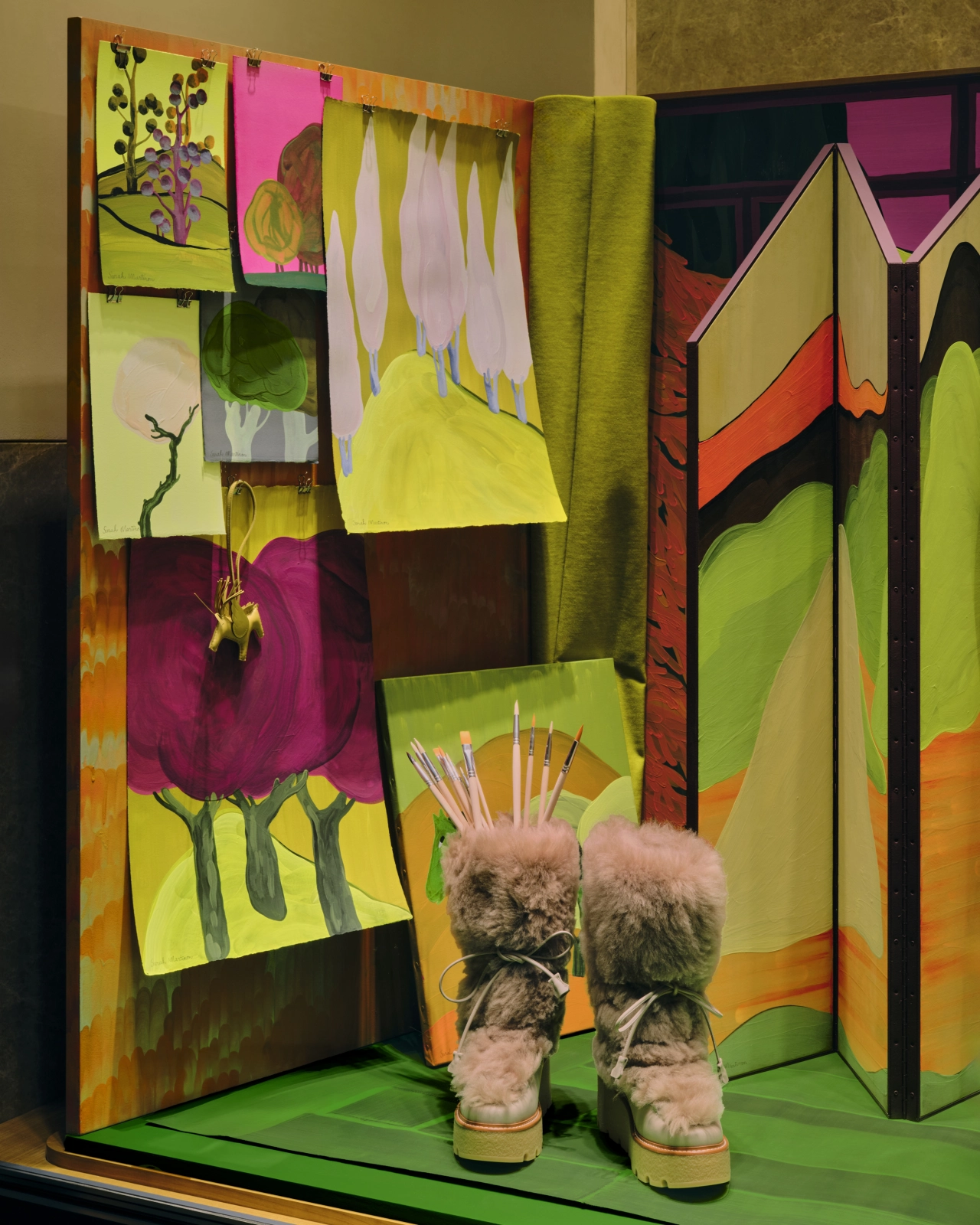 A pair of fluffy platform boots with botanical-inspired artwork displayed in a vibrant window installation featuring colourful drawings and fabric panels in greens, pinks and oranges