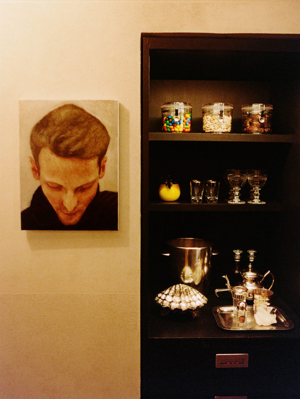 A shelf displaying a still life with a portrait, candy jars, a teapot, and various glassware.