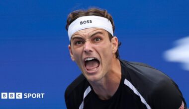Taylor Fritz, wearing a black-and-white T-shirt and white headband, screams during a US Open match