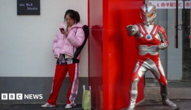 A young woman stands beside a life-sized Ultraman statue outside a shop.