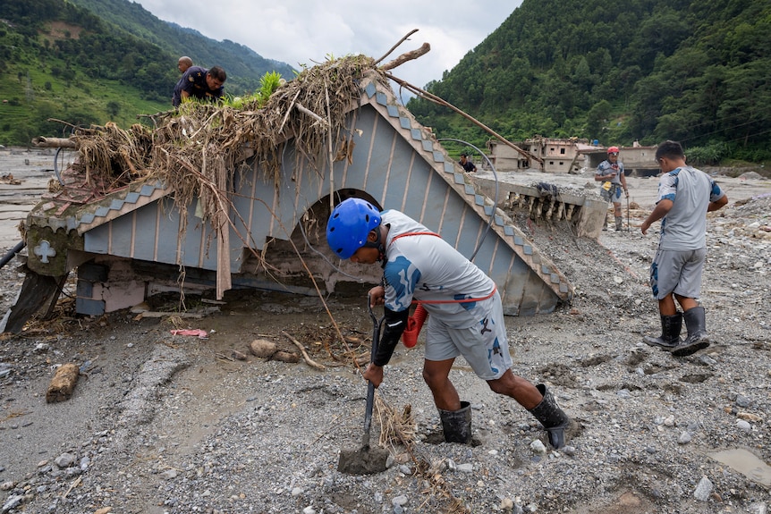 A man digs in thick mud with a sunken house behind him