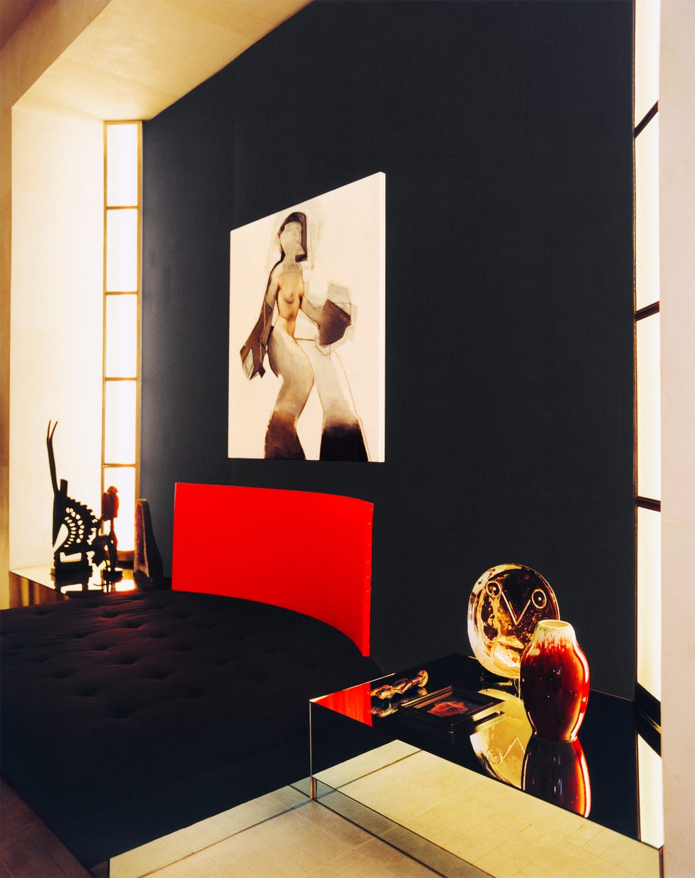 Modern bedroom featuring a red headboard, abstract art, glass furniture, and decorative vases against a dark wall.