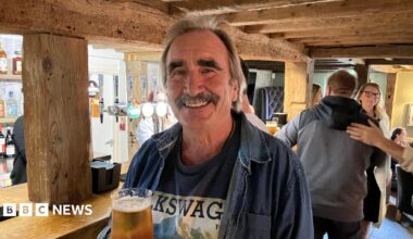 A man with a moustache. He is holding a crisp pint.