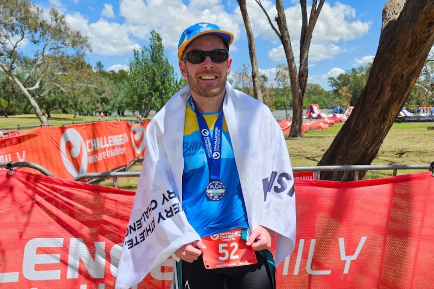 A man in cycling attire, sunglasses and a cap smiles while celebrating after an event.