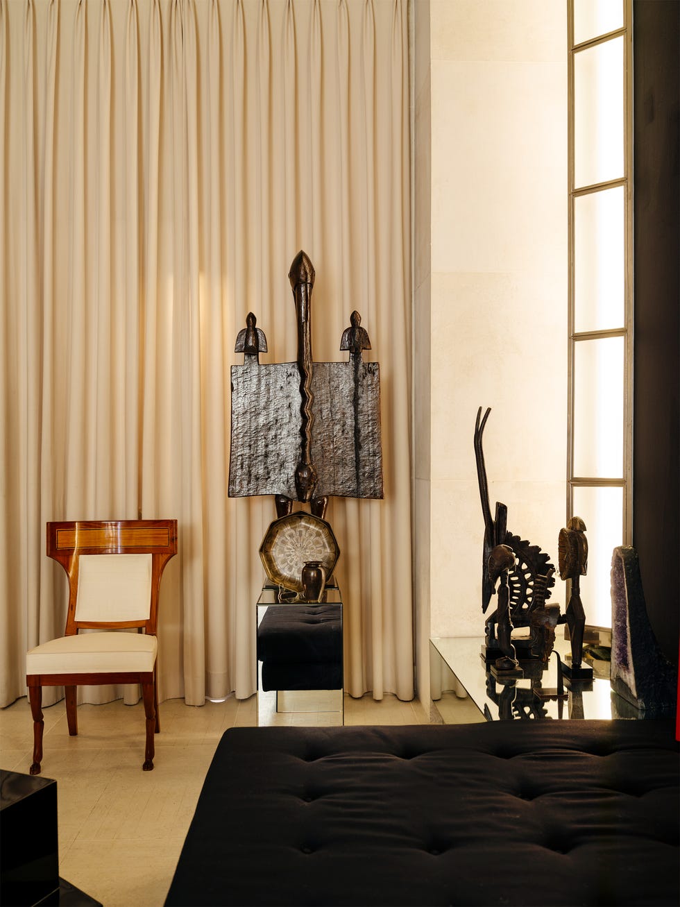 A stylish interior featuring a wooden chair, a decorative arrangement of art pieces, and elegant curtains.