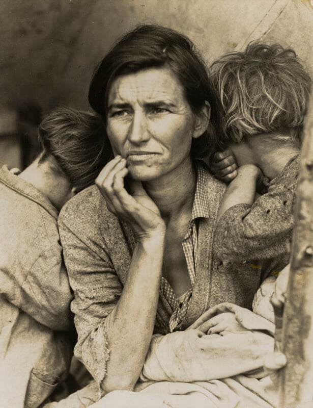 A woman with a weary expression rests her chin on her hand, flanked by two children who have their faces turned away from the camera.