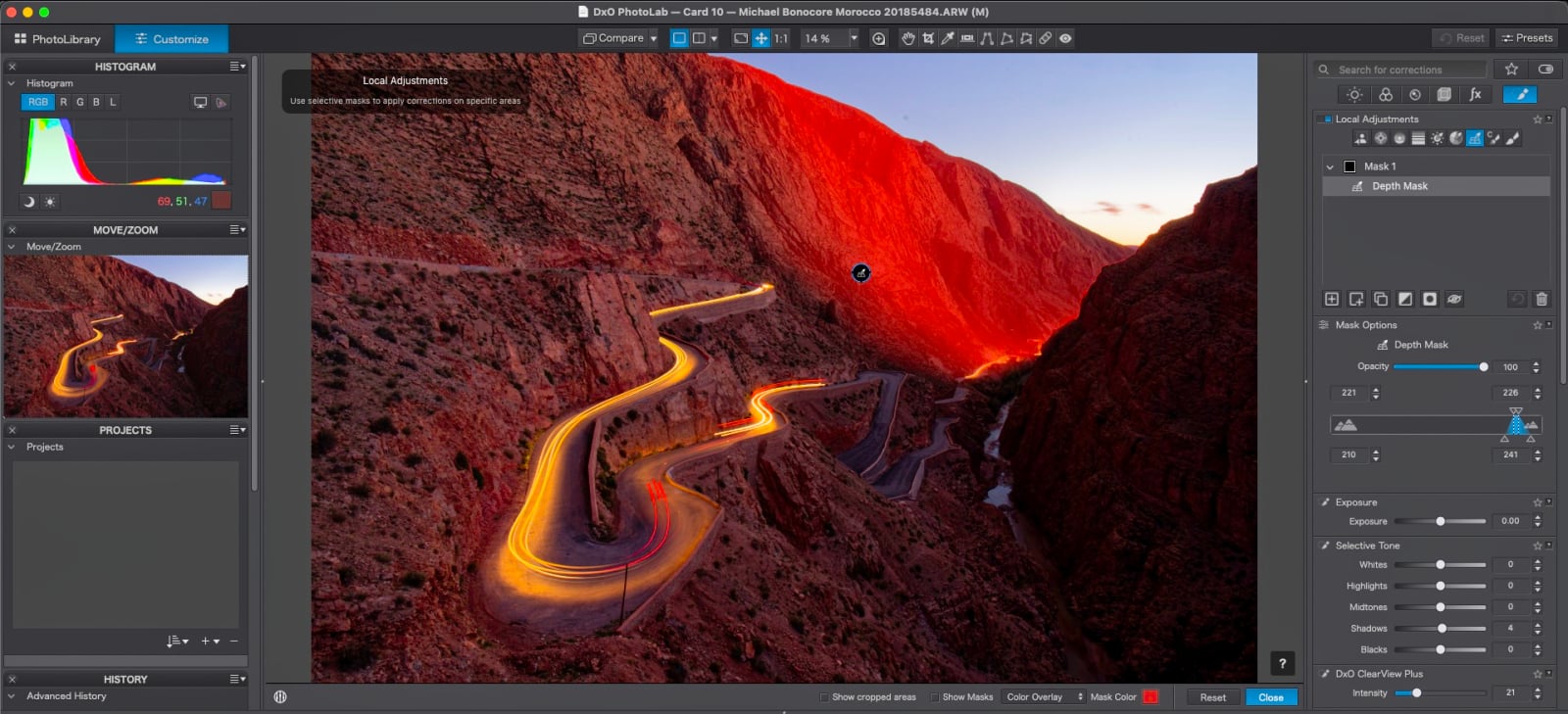 A computer screen displays the DxO PhotoLab software interface, showing a winding road through a canyon with a red mask overlay applied to the mountainside.