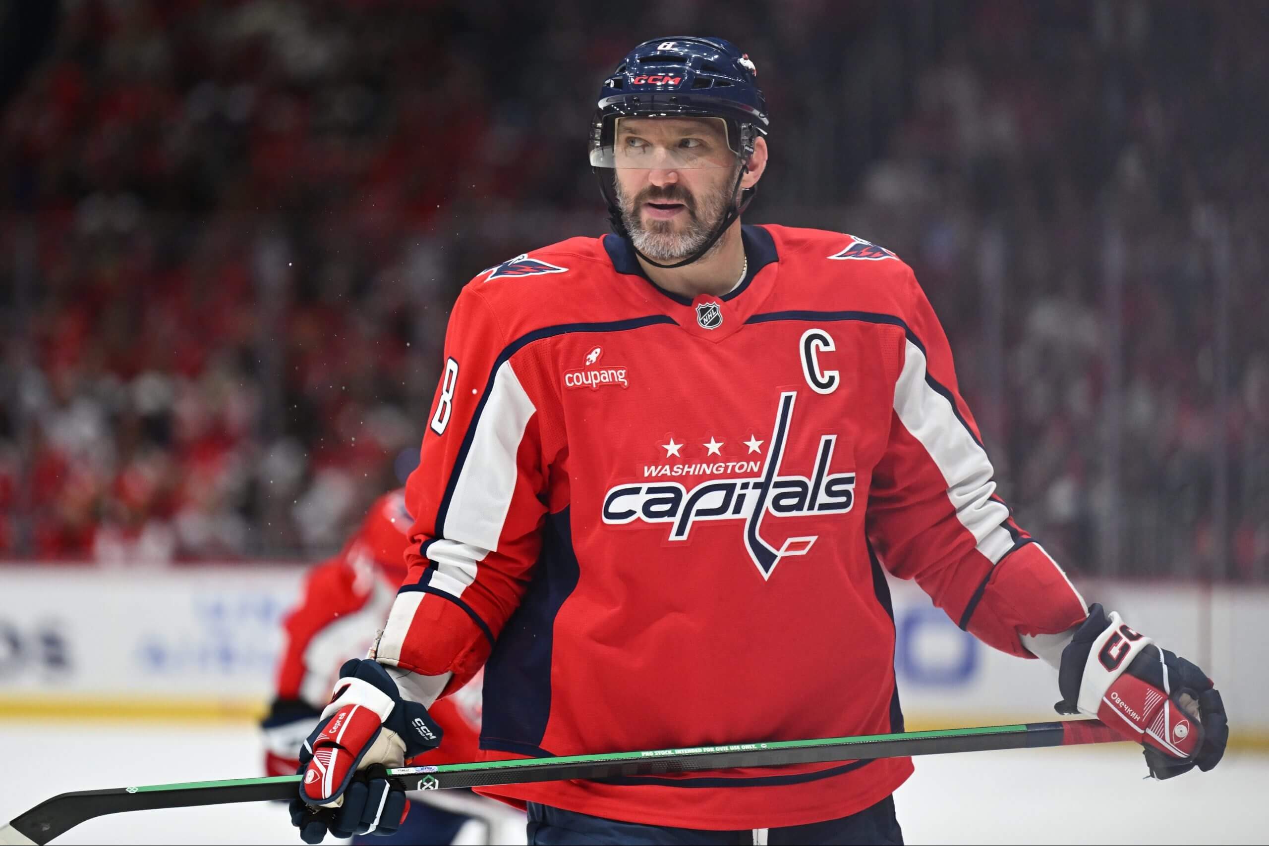 Alex Ovechkin holds onto his stick horizontally with both hands while looking left during a pause in play in a Capitals game.