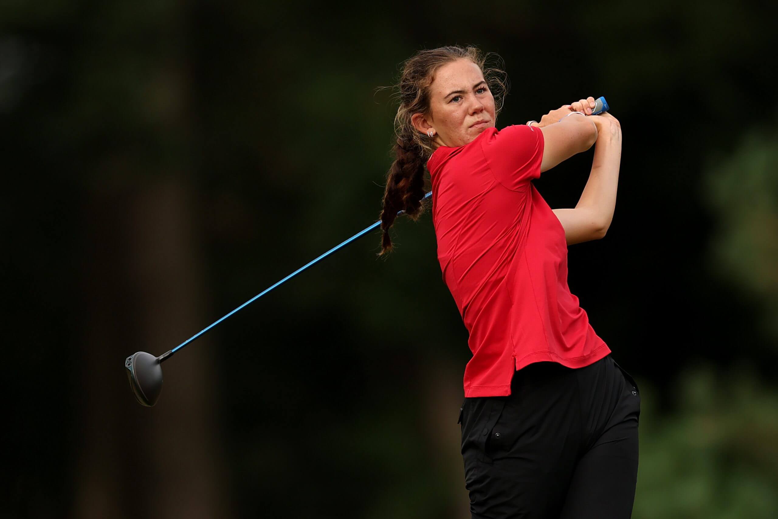 Asterisk Talley, in a red shirt and black pants,  swings a blue club. 