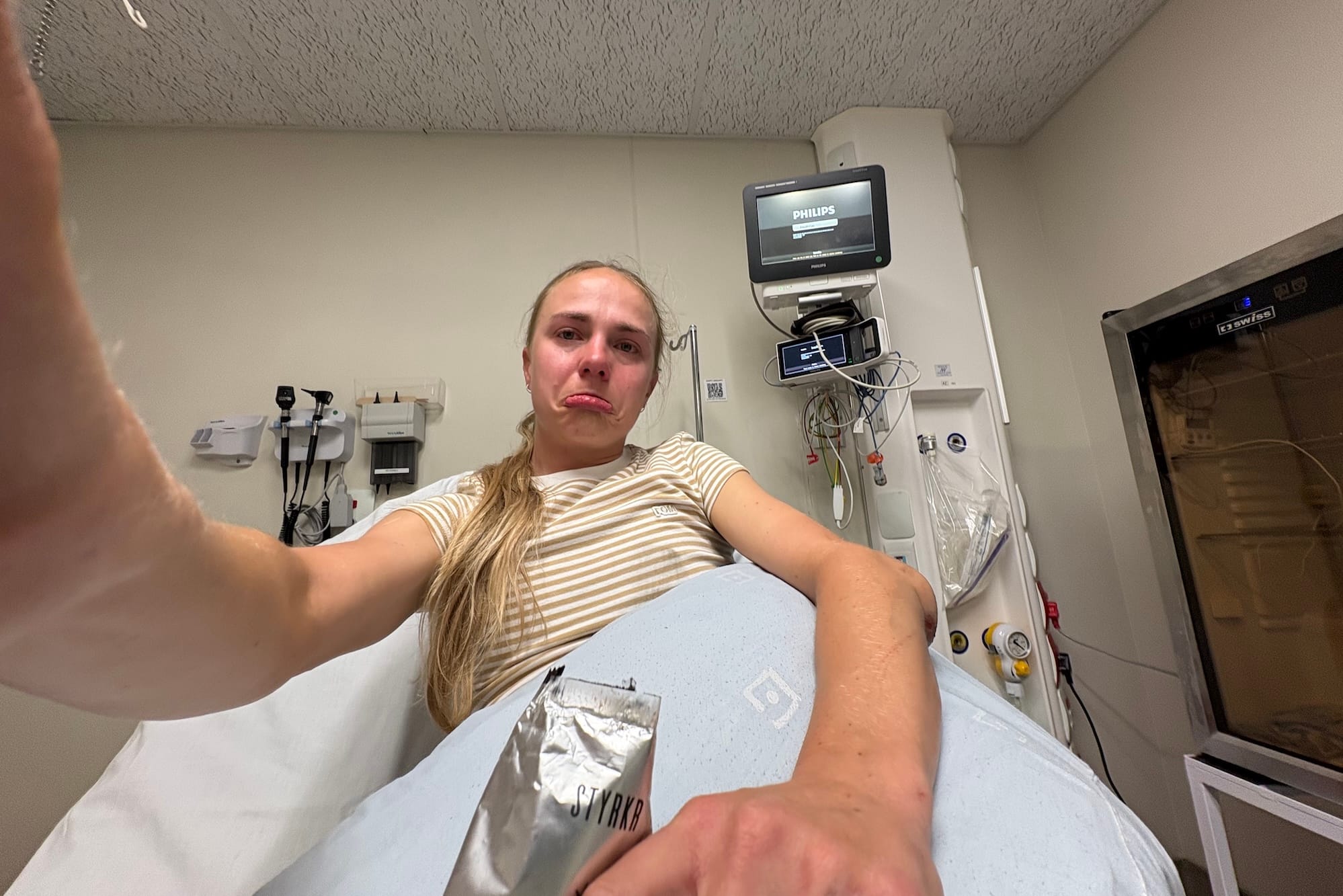 Rollins takes a selfied in a hospital bed with a frown. A huge lump marks the damage to her elbow.