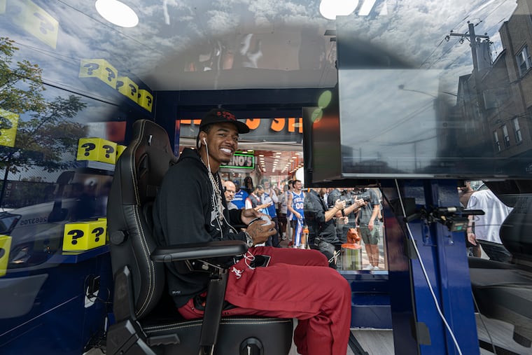 Sixers rookie LaBaron Philon Jr. plays "NBA 2K27" inside a glass gaming truck in front of Geno’s Steaks on Tuesday.