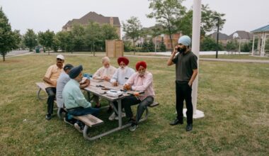 A group of older men sit at a picnic table in a suburban park, while a younger man stands and talks on a cell phone.
