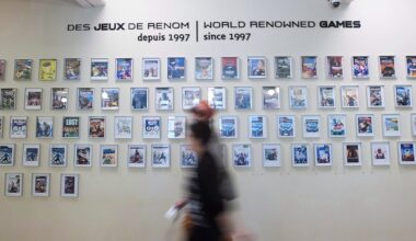 A shot of dozens framed video-game covers on a wall, with the label "World renowned games since 1997" inscribed above them. There are two passers-by blurred in the foreground.