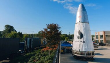 A big white cone with chrome top stands in a parking lot next to a lushes manicured landscape and blue sky.