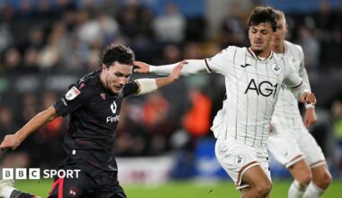 Callum O'Hare of Wrexham shoots as Swansea's Filip Lissah closes down