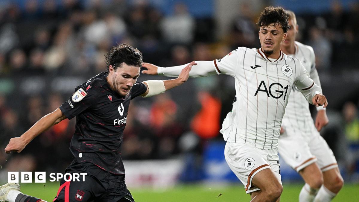 Callum O'Hare of Wrexham shoots as Swansea's Filip Lissah closes down