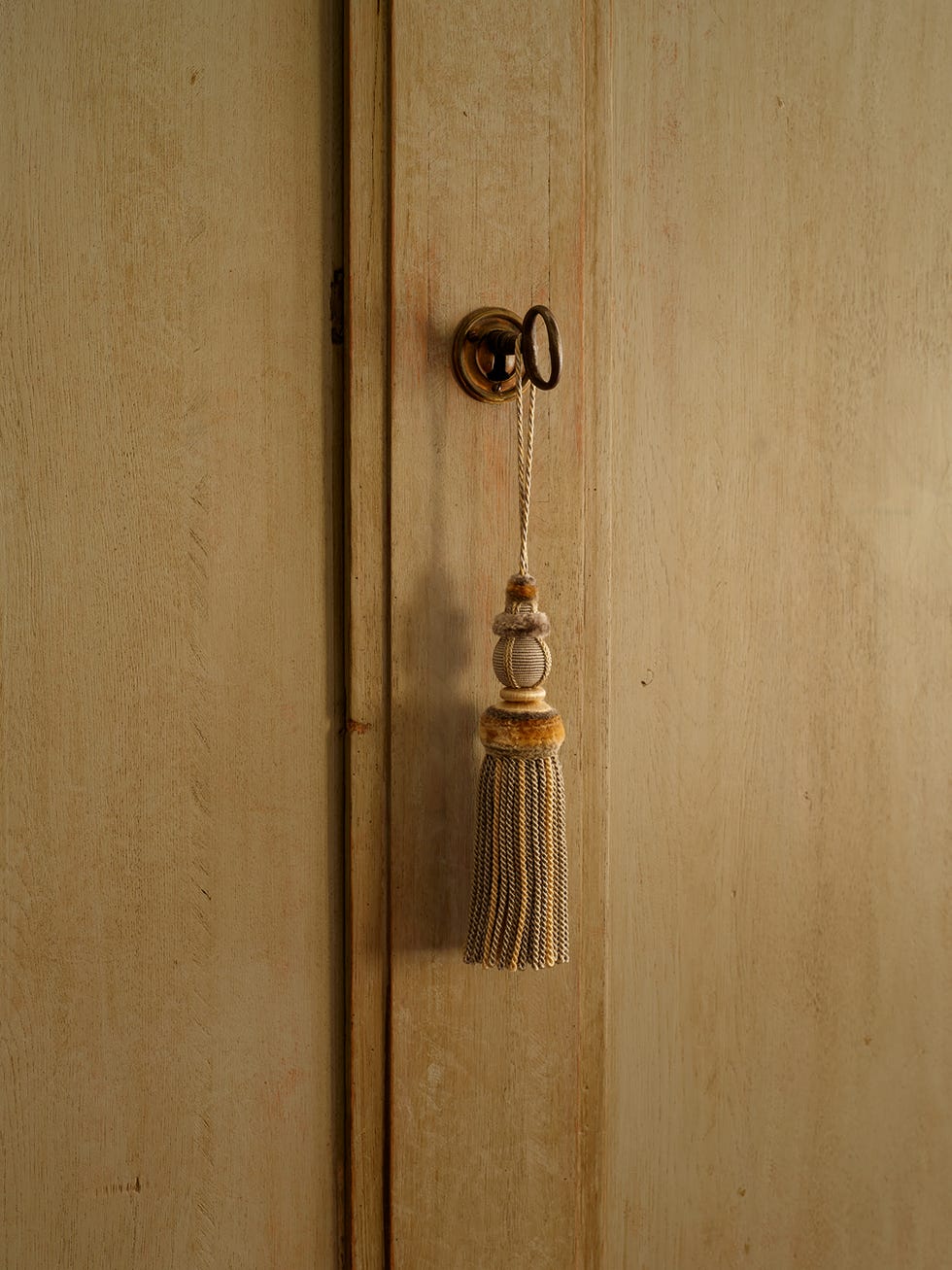 Antique door with a key and ornate tassel hanging from a hook.
