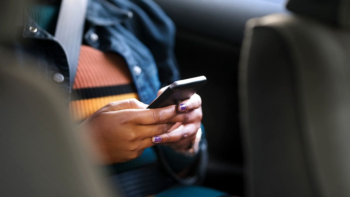 A woman looks at her phone in the backseat of a car.