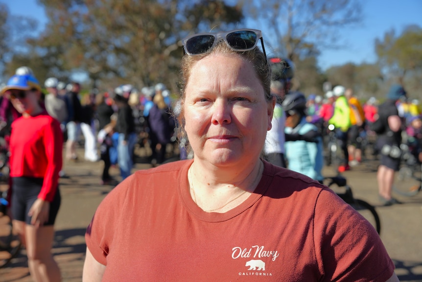 A woman looks seriously into the camera, standing outside.