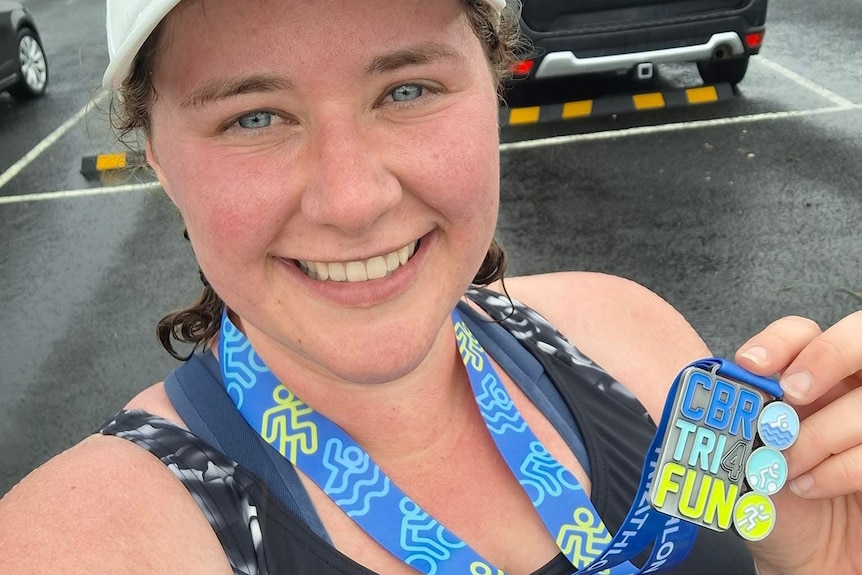 A woman in a white cap after an event smiling holding a blue medal up.