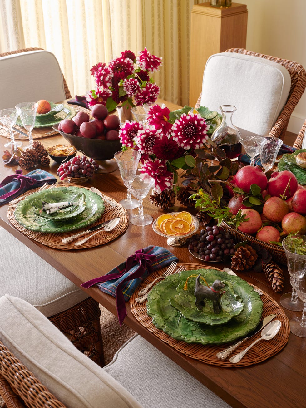 Elegant dining table set with greenery, flowers, fruit, glassware, and decorative plates for a festive gathering.