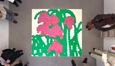 Vibrant hand-cut paper collage featuring bright pink flowers with green stems and leaves against a cream background, viewed from above with people standing around it