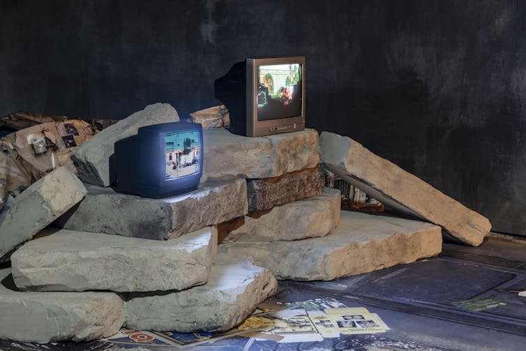 Two TVs on a haphazard stack of stone slates.
