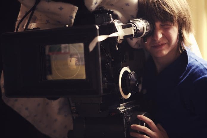 "A young woman operating a 35mm film camera. There is a blanket thrown over the camera to dampen the sound of the film running through it so it doesn't interfere with the scene.Shot on a real set at high iso, some noise, view at 100%.More filmmaking images:"