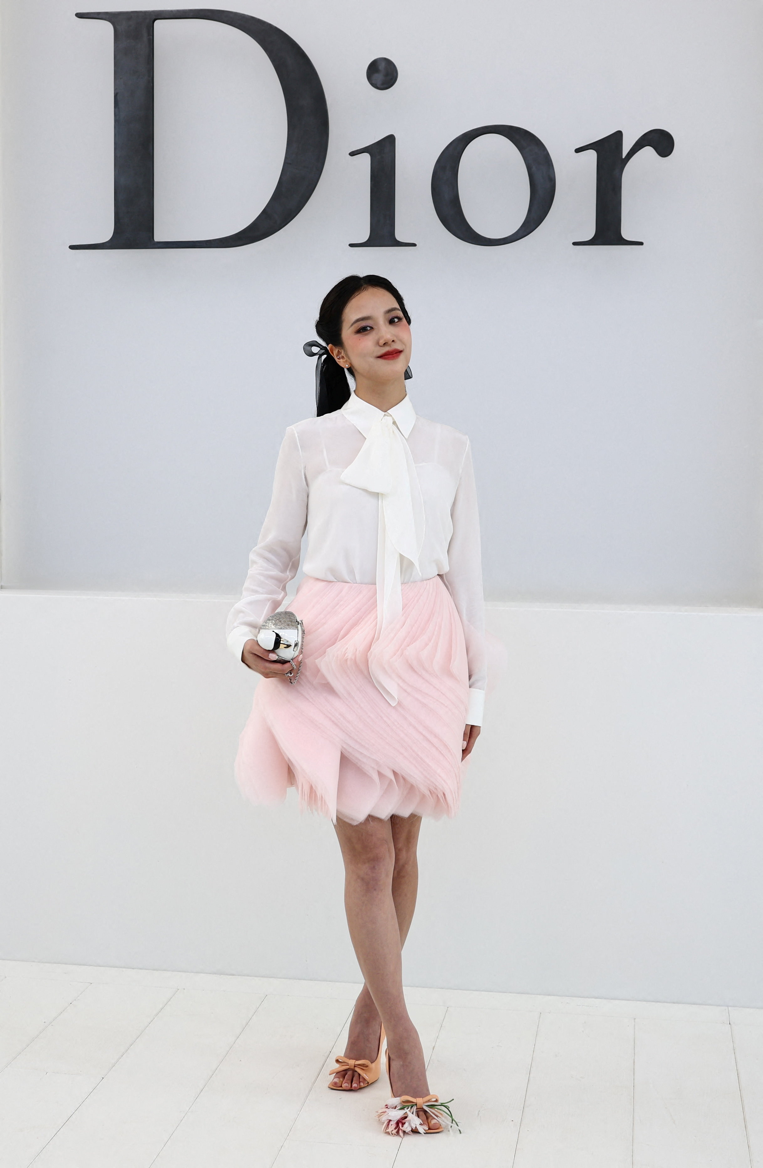 Jisoo posing in a white blouse and pink tiered skirt at the Dior photocall.