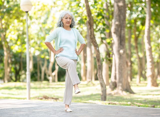 Old age asian woman grandmother put hands on waist raising a leg while walking or exercising in park. Elderly Life, Healthy Living, Chilling Outdoors.