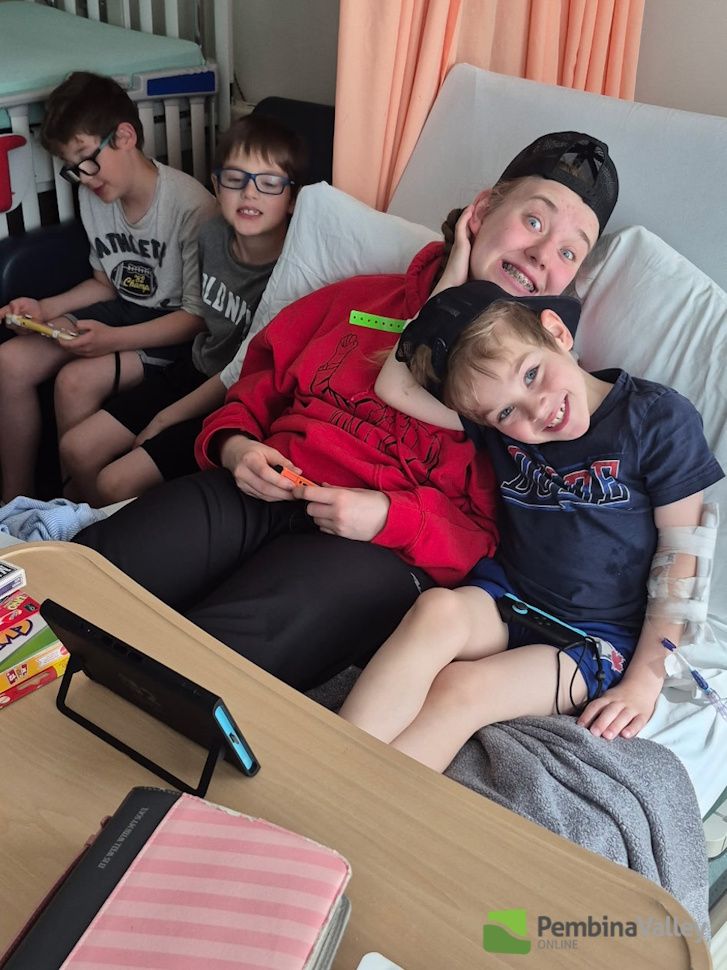 Maverick and Emma in his hospital bed with Tyler and Logan beside them