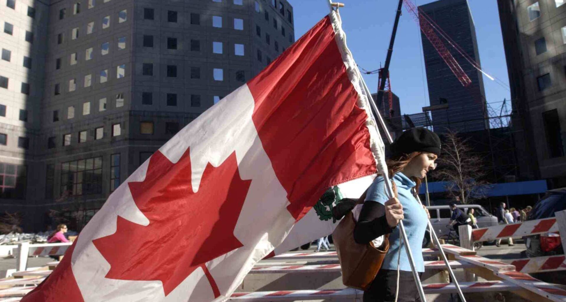 A woman carrying a large Canadian flag walks past Ground Zero in New York.