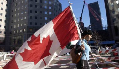 A woman carrying a large Canadian flag walks past Ground Zero in New York.