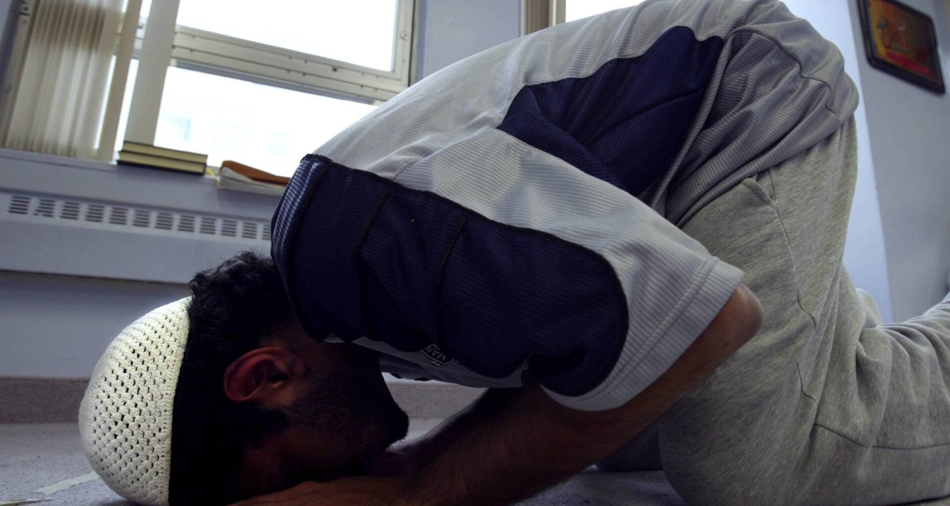 A young man prays next to a window.