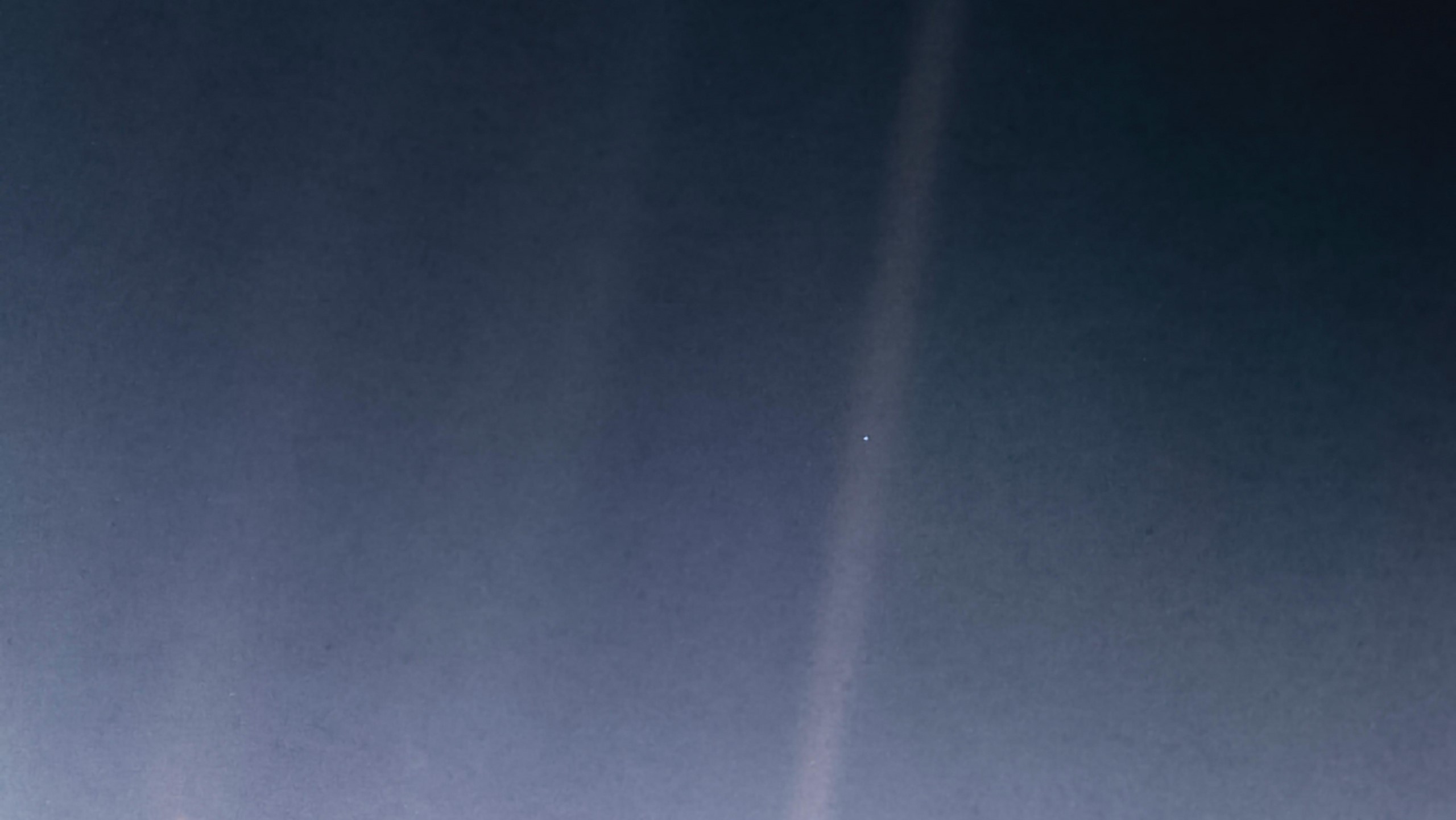 A hazy blueish image has one beam of light in the center-right. There's a tiny blue dot in the beam.